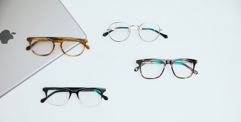 Four pairs of eyeglasses next to a laptop