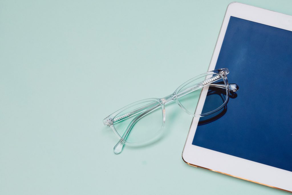 A pair of clear eyeglasses on a white iPad over a mint green background