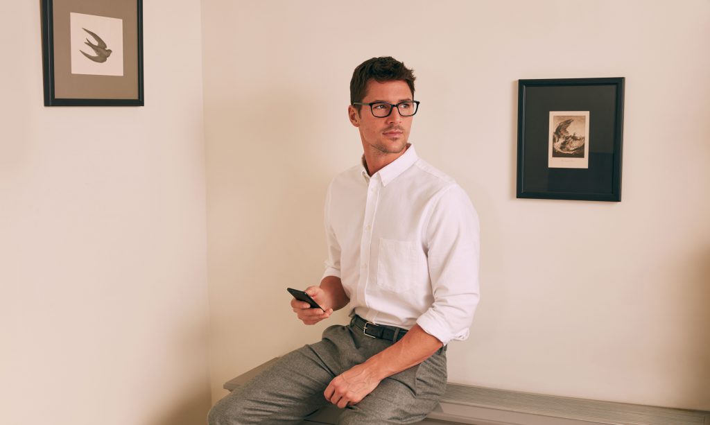 Man wearing Felix Gray blue light glasses with phone sitting on a table