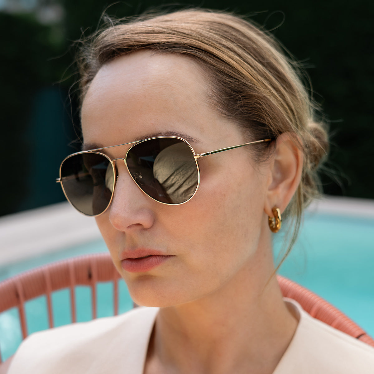 Woman by pool wearing gold aviator sunglasses with grey lenses