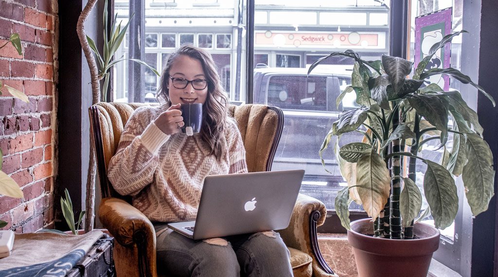 Rebecca Working Wearing Her Felix Gray Glasses holding up a tea working on her computer