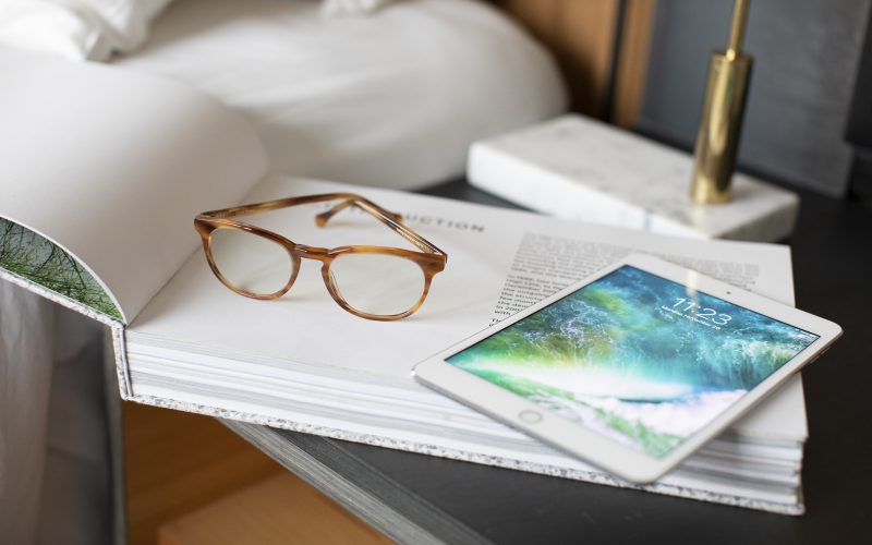 Brown Roebling glasses and iPad on a book on a bedside table