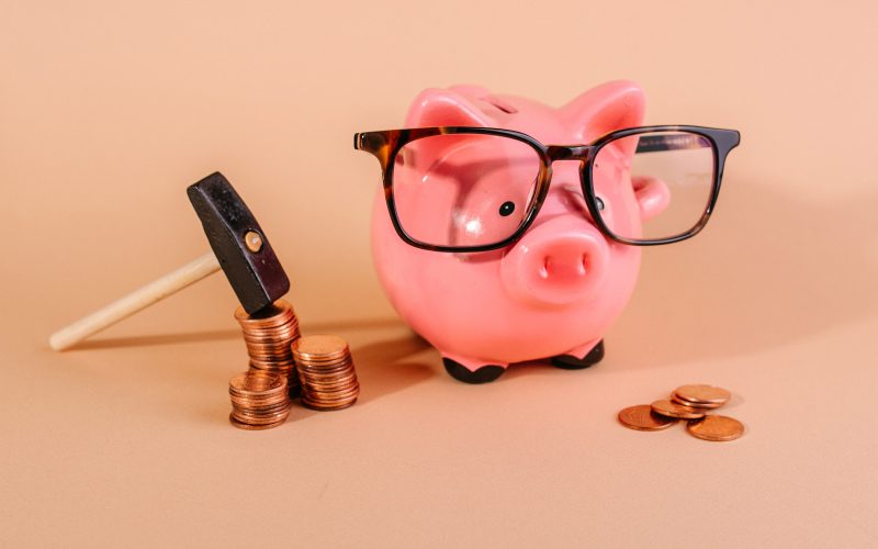 A piggy bank wearing Felix Gray glasses next to a pile of pennies