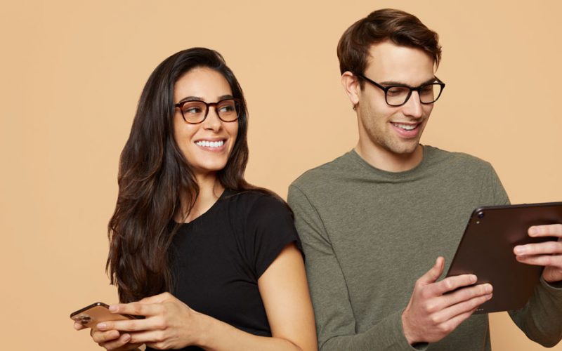 Woman wearing eyeglasses looking at her phone and man wearing glasses looking at his iPad