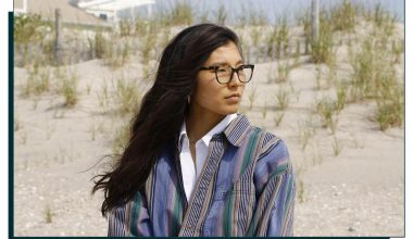 Woman sitting at the beach looking to the right wearing glasses