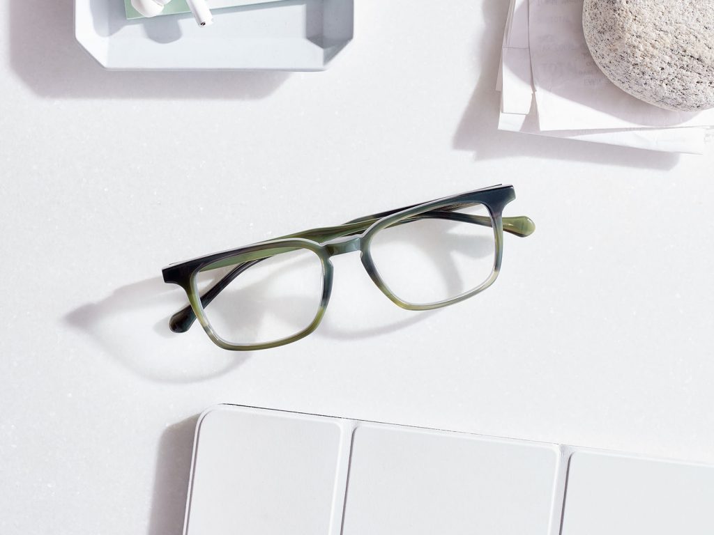 Green square eyeglasses on a desk with other items in the corners