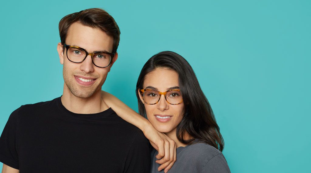 Man and woman side by side wearing glasses on a teal backgorund