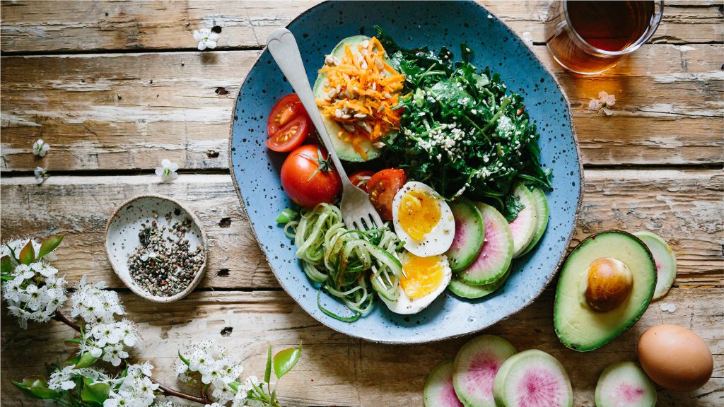 Salad on a wooden table with a drink and flowers